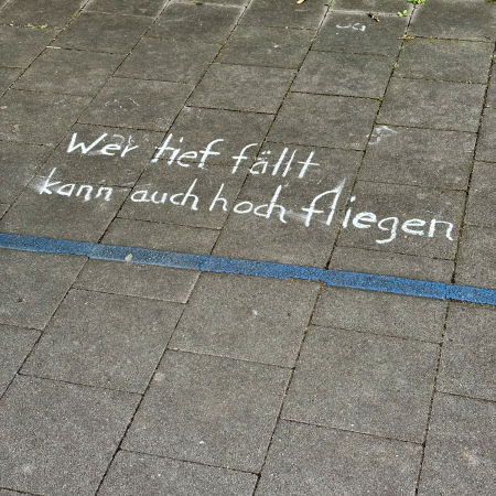 Kreideschrift auf dem Pflaster: Wer tief fällt kann auch hoch fliegen