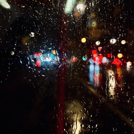 Blick durch eine nasse Scheibe in die Großstadtnacht, verschwommene bunte Lichter im Dunkeln