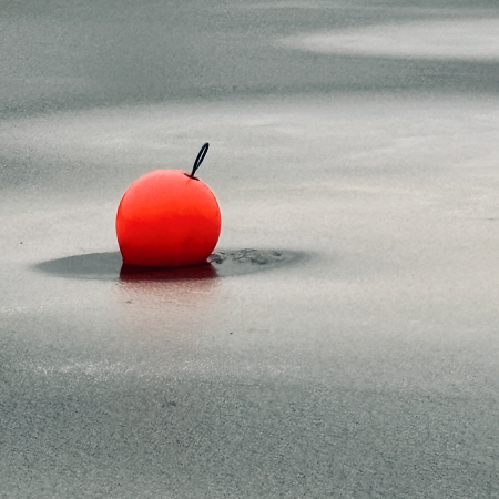Eine hellrot leuchtende Boje im Alstereis