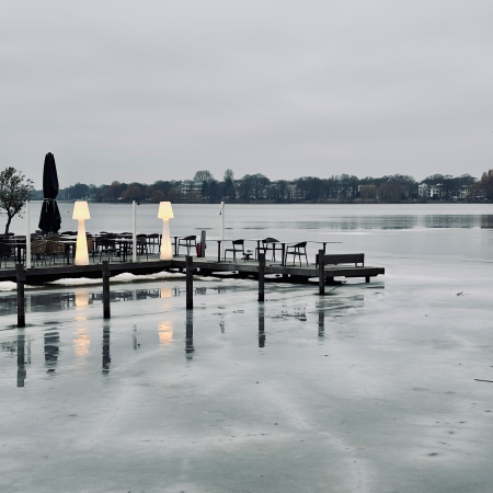 Ein Steg an der Außenalster, mit leerer Außengastro-Bestuhlung vor vereister Kulisse