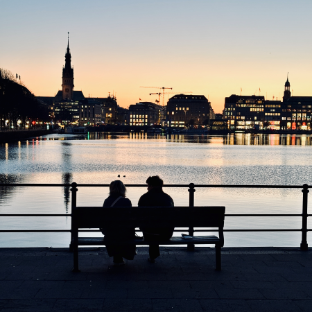 Ein Paar auf einer Bank von hinten fotografiert, vor der abendlichen Binnenalster