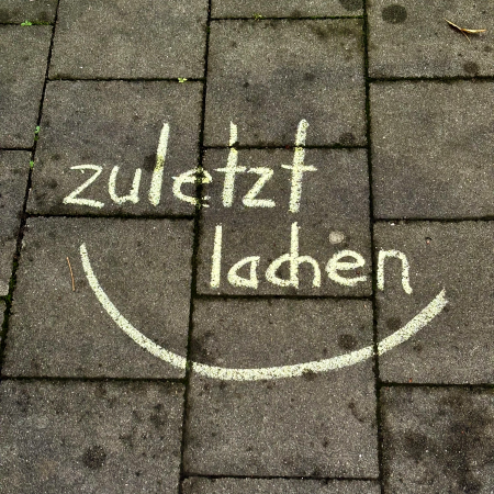 Kreideschrift auf dem Pflaster: zuletzt lachen