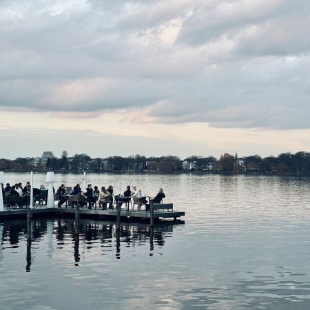 Ein Steg mit Außengastro darauf an der Außenalster