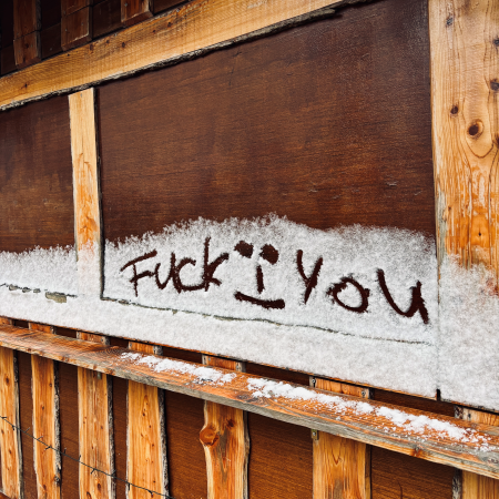 Jemand hat "Fuck you" in Schneereste an der Wand einer Bretterbude für Glühweinausschank geschrieben