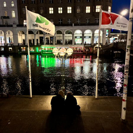 Ein Paar, von hinten fotografiert, sitzt auf den Stufen gegenüber den Arkaden an der Kleinen Alster