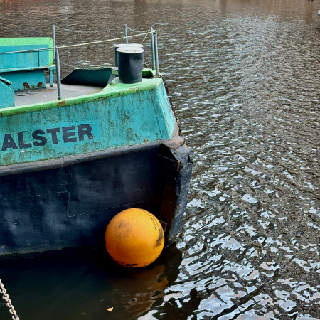 Der Bug einer Schute mit dem Namenszug "Alster" und einem Fender in leuchtendem Orange