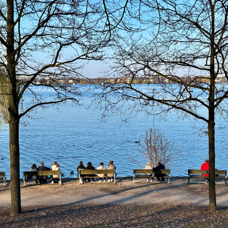 Menschen auf Bänken an der Aupßenalster, von hinten aufgenommen