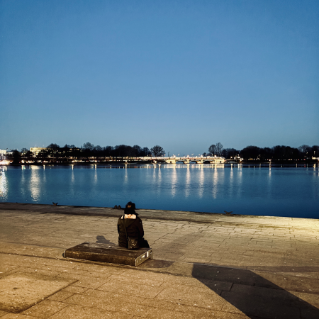 Ein Mann sitzt am Abend am Jungfernstieg auf einer der Bänke und sieht auf die Binnenalster