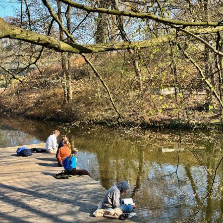 Menschen in Planten un Blomen, die am Wasser in der Sonne sitzen und teils lesen