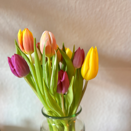Ein Strauß bunter Tulpen in einer Glasvase vor Raufaser