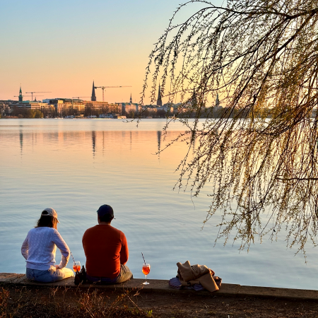 Menschen am Ufer der Außenalster sitzend, Aperolgläser neben ihnen
