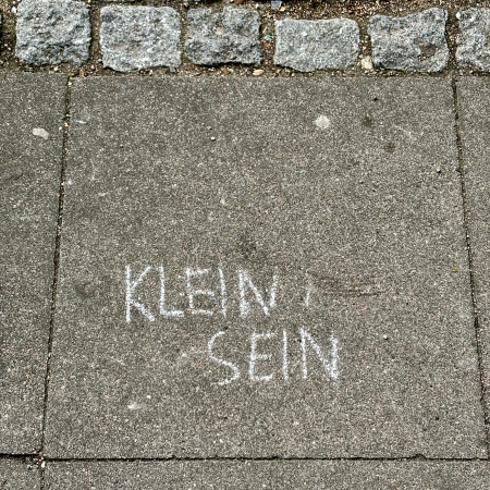 Kreideschrift auf dem Pflaster: Klein sein