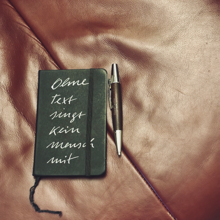 Ein Notizbuch mit Aufschrift "Ohne Text singt kein Mensch mit"
