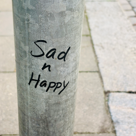 Eddingschrift an einem Verkehrsschildmast: "Sad n happy"