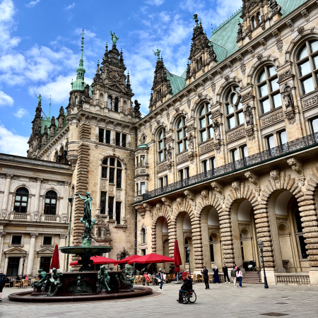 Der Brunnen im Innenhof des Rathauses, blauer Himmel, rote Sonnenschirme der Außengastro