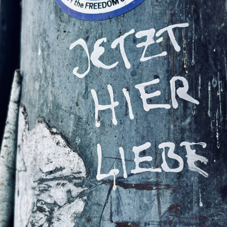 Weiße Schrift auf einem Ampelmast: Jetzt hier Liebe