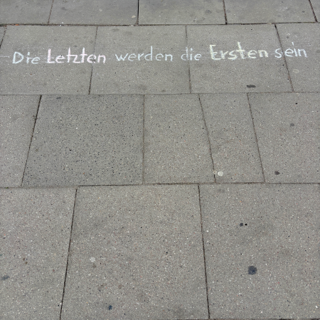 Kreideschrift auf dem Pflaster: Die Letzten werden die Ersten sein.