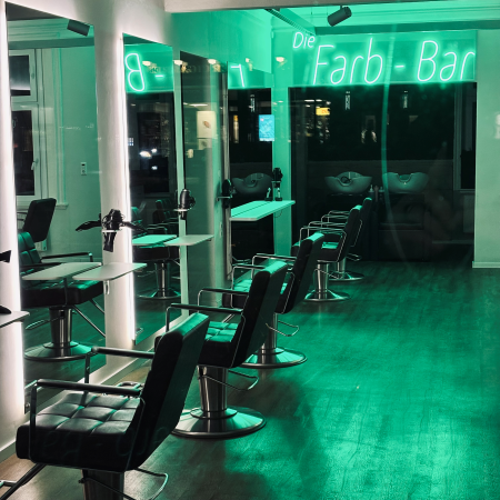Ein Frisieralon abends, grünes Licht, an der Wand der Neon-Schriftzug "Farb-Bar"