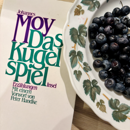 Das Buch "Das Kugelspiel" neben einem Teller mit Heidelbeeren