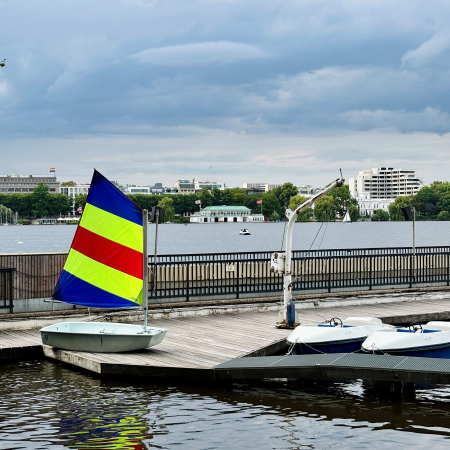 Ein kleines Segelboote mit sehr buntleuchtendem Segel auf einem Steg an der Außenalster