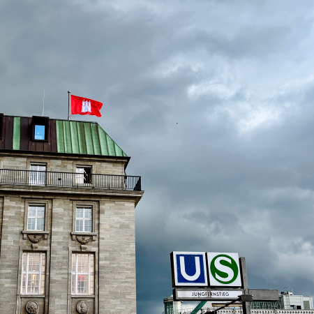 Auf dem "Uniqlo"-Gebäude am Rathausmarkt weht eine Hamburg-Flagge, die sich sehr rot vom regnerischen Himmel abhebt
