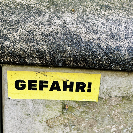 Ein Sticker auf grauem Beton, es steht "Gefahr!" darauf