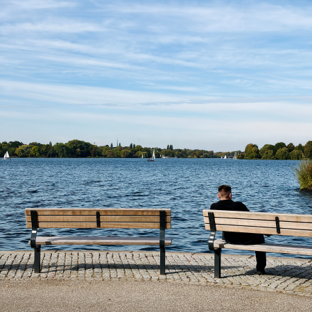 Ein Mensch auf einer Bank an der Außenalster, von hinten gesehen