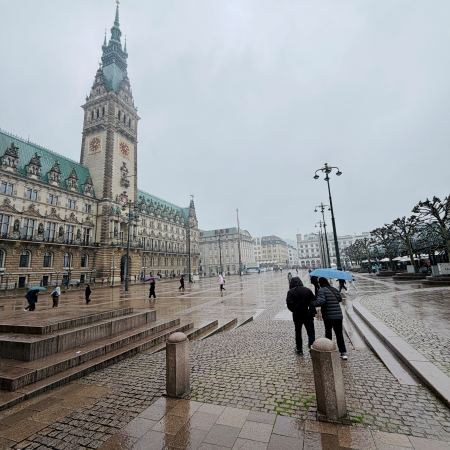 Der Rathausmarkt, größtenteils menschenleer, bei Wind und Regen, im Vordergrund Menschen mit Regenschirm