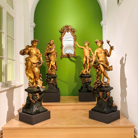 Goldene Skulpturen vor grüner Wand im Museum